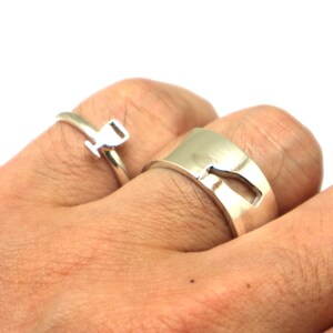 May include: Two silver rings, one with a simple design and the other with a cutout shape. The rings are worn on a person's fingers.