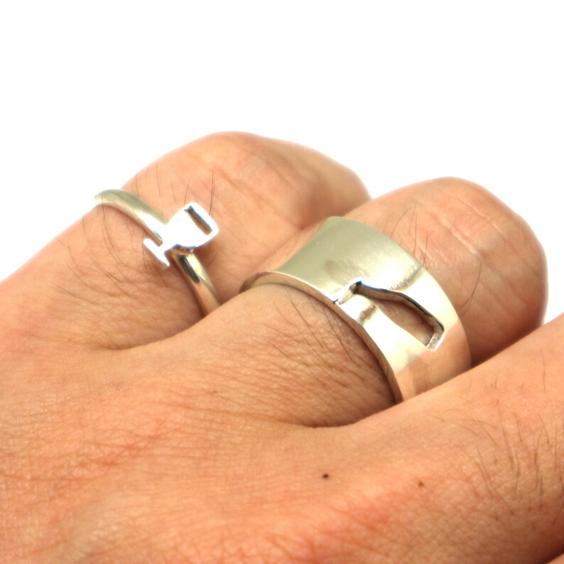 May include: Two silver rings, one with a simple design and the other with a cutout shape. The rings are worn on a person's fingers.
