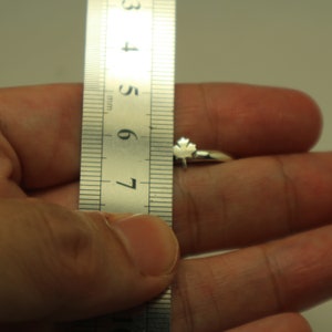May include: A silver ring with a maple leaf design. The ring is shown next to a ruler, with the ring's total length measuring approximately 0.5 inches.