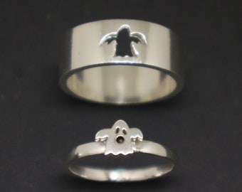 May include: Two silver rings with a ghost cutout design. The top ring has a ghost cutout, while the bottom ring has a ghost design on the top.
