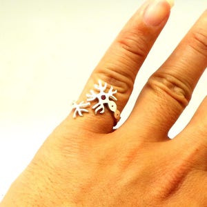 May include: A silver ring with a red gemstone in the center, shaped like a stylized neuron.