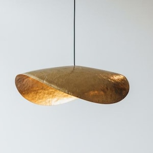 May include: A contemporary, gold-coloured pendant light hangs above a round wooden table. The light has a distinctive, curved shape and illuminates the space. Two wooden chairs with woven seats are positioned near the table, creating a minimalist dining area.