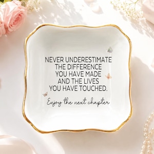 May include: A square white ceramic trinket dish with scalloped edges and a gold-painted rim. The center features black text reading: NEVER UNDERESTIMATE THE DIFFERENCE YOU HAVE MADE AND THE LIVES YOU HAVE TOUCHED. Enjoy the next chapter, with small butterflies.