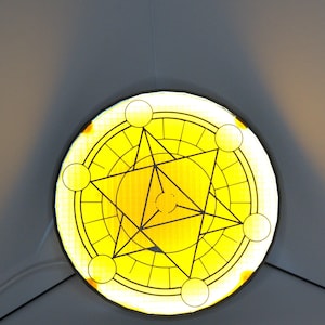 May include: A round, yellow stained glass window with a geometric design. The design features a central star within a circle, surrounded by smaller circles and lines. The window is illuminated, creating a warm glow.