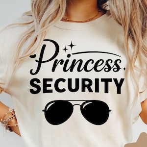 Puede incluir: Sudadera color crema con las palabras "Princess SECURITY" en escritura negra y letras mayúsculas en negrita. Debajo del texto hay una silueta negra de gafas de sol. La sudadera es de estilo casual.