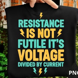 May include: Black t-shirt with the text "RESISTANCE IS NOT FUTILE IT'S VOLTAGE DIVIDED BY CURRENT" in teal and yellow. The design includes lightning bolt graphics. The shirt is held up by a hand.