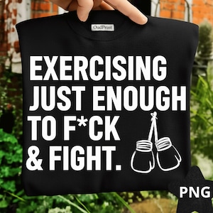May include: Black sweatshirt with the text "EXERCISING JUST ENOUGH TO F*CK & FIGHT." in white, along with a graphic of two boxing gloves. The sweatshirt is held up by a hand.