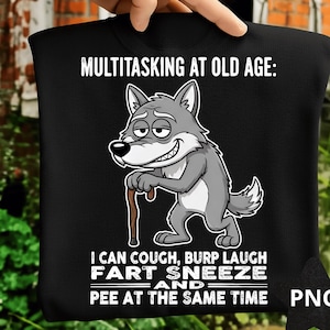 May include: Black t-shirt featuring the text "MULTITASKING AT OLD AGE: I CAN COUGH, BURP LAUGH FART SNEEZE AND PEE AT THE SAME TIME" and a cartoon wolf with a walking stick. The wolf is grey and white.