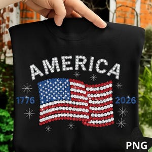 May include: Black sweatshirt with the word "AMERICA" in white, sparkling letters. Below, a sparkling American flag design in red, white, and blue. The numbers "1776" and "2026" are on either side of the flag, with star accents.