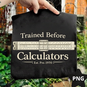 Puede incluir: Bolso tote negro con el texto "Trained Before Calculators" y un gráfico de regla de cálculo. El texto "Est. Pre-1970" está debajo. El bolso es sostenido por una mano.