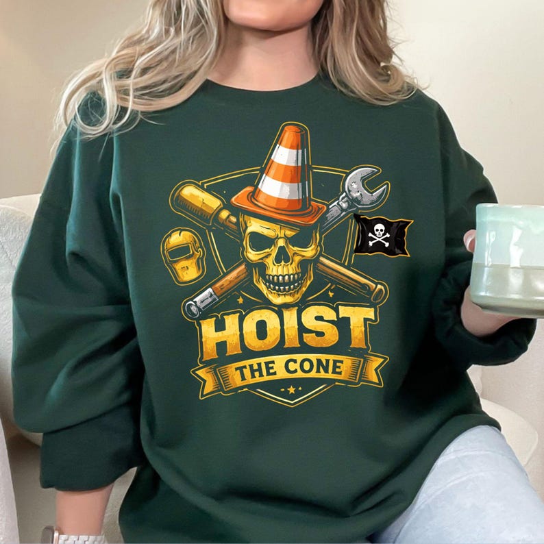 May include: Dark green sweatshirt with a graphic featuring a skull wearing an orange traffic cone, crossed tools, and a pirate flag. The text "HOIST THE CONE" is displayed in gold lettering on a banner.