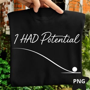 May include: Black sweatshirt with the white text "I HAD Potential" in a cursive font. Below the text is a white curved line with a white circle at the end, resembling a golf ball. The sweatshirt is held by a hand.