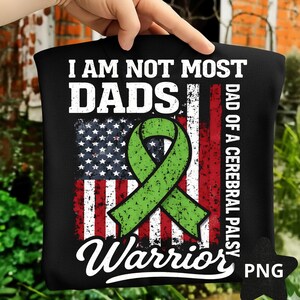 Op de afbeelding: Zwart T-shirt met een verweerd Amerikaans vlagontwerp, een groen lint en de tekst "I AM NOT MOST DADS, DAD OF A CEREBRAL PALSY WARRIOR". Het ontwerp is in wit en groen.