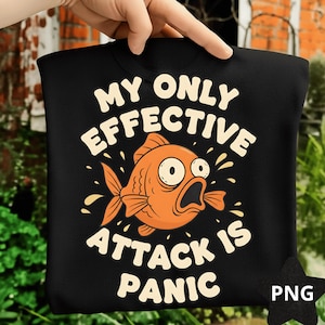 Può includere: Felpa nera con la scritta bianca "MY ONLY EFFECTIVE ATTACK IS PANIC", con un'illustrazione di pesce rosso arancione. Il pesce ha grandi occhi e la bocca aperta. La felpa è tenuta da una mano.
