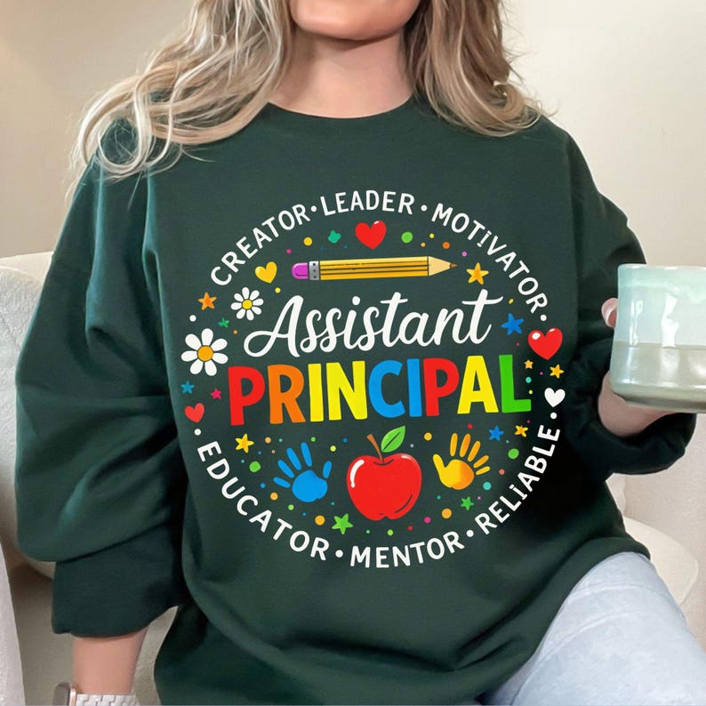 May include: Dark green sweatshirt featuring the words "Assistant Principal" in vibrant colours. The design includes a pencil, apple, handprints, and the words "Creator, Leader, Motivator, Educator, Mentor, Reliable" in a circle.