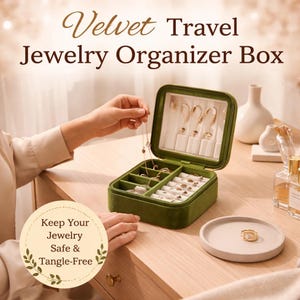 May include: A green velvet travel jewelry organiser box with multiple compartments. The box is open, displaying necklaces and earrings. The text on the box reads "Velvet Travel Jewelry Organizer Box". A small plate with a ring is on the table.