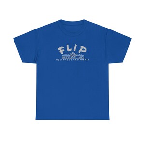 May include: A royal blue t-shirt with a crew neck. The shirt features the text "FLIP" in a stylized font above the text "RECORDS, INC." and "HOLLYWOOD CALIFORNIA" in a rectangular box. The text is in a light gray color.