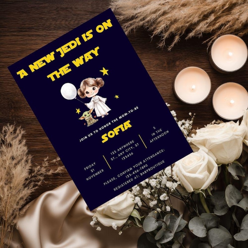 Star Wars baby shower invitation displayed in a white frame on a wooden table, featuring chibi Princess Leia holding a balloon and Baby Yoda on a navy galaxy background with gold text 'A New Jedi is on the Way'.