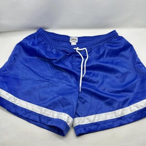 May include: Royal blue athletic shorts with white stripes along the bottom hem. The shorts have a white drawstring and a small tag at the waistband. The shorts are made of a shiny, lightweight material.