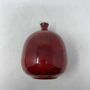 May include: A glossy, deep red ceramic vase with a rounded body and a narrow neck. The vase has a smooth, reflective surface, and the color is a rich, dark shade of red. The vase is a decorative item.