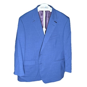 Può includere: Un blazer blu con un sottile motivo a quadri, appeso a una gruccia bianca. Il blazer ha una chiusura a due bottoni, revers a lancia e fodera viola. La gruccia ha il testo "iSteamer" stampato.