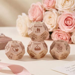 May include: A set of wooden activity dice with engraved icons and text, such as "Romance," "Take a Walk," and "Chinses." The dice are light brown and feature various activity suggestions. A bouquet of pink roses is in the background.