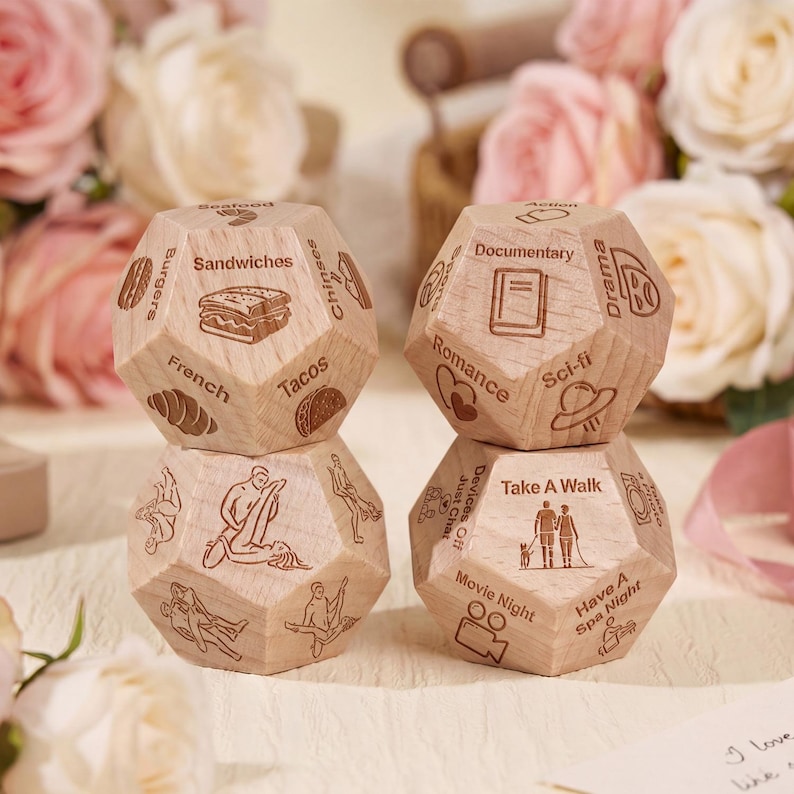 May include: Four wooden dice with engraved text and illustrations. The dice feature options like "Sandwiches," "Romance," and "Take a Walk." The dice are light brown and sit in front of a blurred floral background.
