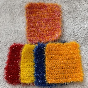 Könnte beinhalten: Eine Sammlung farbenfroher, quadratischer, gehäkelter Schwämme. Die Schwämme sind in den Farben Rot, Gelb, Blau und Orange gehalten. Ein Schwamm ist eine Mischung aus Orange und Rosa. Die Schwämme haben ein strukturiertes, flauschiges Aussehen.