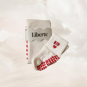 May include: A pair of off-white ribbed socks with red heart-shaped grip patterns on the soles. One sock features the embroidered red text MINI above a small red heart. A grey paper band with the black text Liberte is wrapped around the socks.