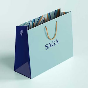 K&ouml;nnte beinhalten: Hellblaue Einkaufstasche mit dem Aufdruck "SAGA" auf der Vorderseite. Die Tasche hat einen dunkelblauen Boden und orangefarbene Kordelgriffe. Die Innenseite weist ein Streifenmuster in Blau-, Orange- und Wei&szlig;t&ouml;nen auf.