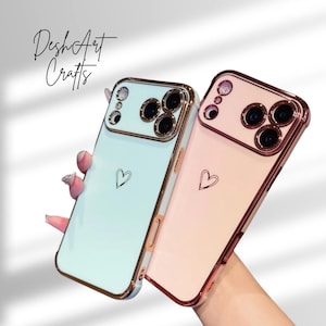 May include: Two phone cases, one light blue and one pink, with gold-colored trim. Each case has a small heart design and a camera cutout. The text "DeshArt Crafts" is written in cursive on the top left.