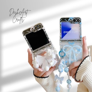 Puede incluir: Fundas transparentes para teléfonos con elementos decorativos. Una funda presenta un lazo blanco y detalles de perlas, la otra un lazo azul y un dije de cuentas. Las fundas están abiertas, revelando las pantallas de los teléfonos. El texto "DeshArt Crafts" es visible.