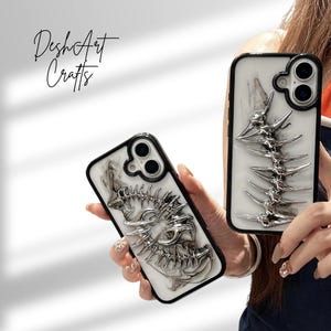 May include: Two phone cases with a white and black marble design and a silver spine-like embellishment. The cases have a black border and a camera cutout. The text "DeshArt Crafts" is in the upper left corner.