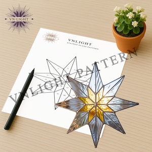 May include: A stained glass star with a gold center and blue-gray points sits next to a pattern diagram. The diagram is labeled "VNLIGHT STAINED GLASS PATTERN". A black pen and a small potted plant are also in the image.