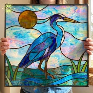 May include: Stained glass panel featuring a blue heron standing in water with green reeds. The artwork includes a yellow sun and a sky of blue, purple, and white. The panel is framed in a dark metal.