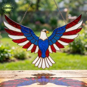 May include: Stained glass eagle with outstretched wings, featuring red, white, and blue colors. The patriotic design includes stripes and a central blue area, hanging from a chain. The eagle's beak is yellow, and the wings are spread wide.