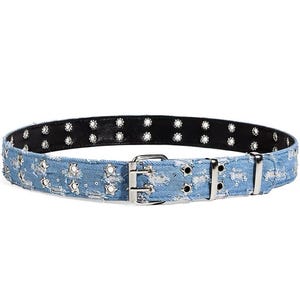 May include: A light blue denim belt featuring a repeating pattern of silver-toned star-shaped studs and circular grommets. The belt includes a double-prong metal buckle and a black interior lining, showcasing a rugged texture throughout the design.