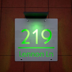 以下が含まれることがあります： 明るい緑色で「219」の数字と「Lennon Ln」のストリート名が表示された、白い背景の照明付き住所標識。レンガの壁に取り付けられており、上部は黒色です。