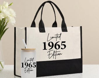 Op de afbeelding: Een crèmekleurige canvas draagtas met zwarte handvatten en een zwarte basis. De tas heeft de tekst "Limited 1965 Edition". Een matglazen tumbler met een rietje en houten deksel staat voor de tas, eveneens met de tekst "Limited 1965 Edition".