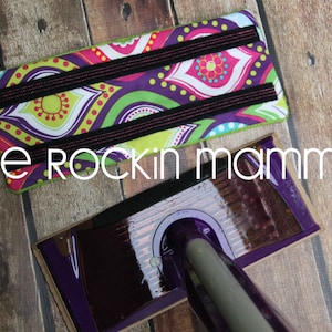 May include: A colorful fabric pad with black elastic straps, designed to fit a cleaning tool. The pad has a paisley pattern with green, purple, pink, and yellow colors. The text "one rockin mamma" is visible below the pad.