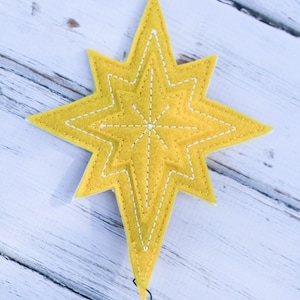May include: A yellow felt star with white stitching, designed to be used as a Christmas tree topper. The star has a wire attached to the bottom for easy placement.