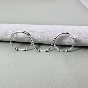 May include: A silver ring featuring an infinity symbol design. The ring has two circular bands linked by a figure-eight shape. The ring is made of a shiny, reflective metal.
