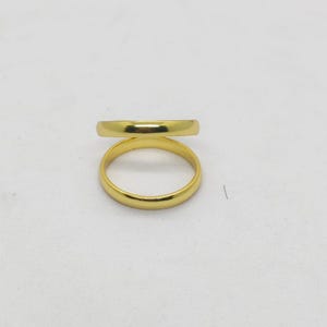 May include: Two gold wedding bands are stacked on a white surface. The rings are a simple, classic design with a smooth, polished finish. The bands are a bright, shiny gold color.