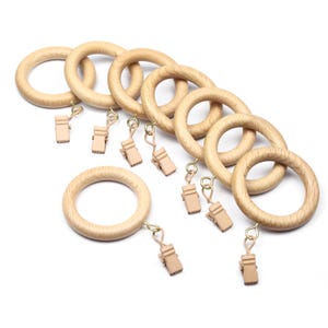 May include: A collection of wooden curtain rings with attached clips. The rings are light brown and have a smooth finish. The clips are a light tan color and are attached to the rings with small metal hooks. The items are arranged on a white background.