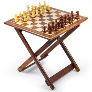 May include: A wooden folding chess table with a checkered playing surface. The chess pieces are arranged on the board, ready for a game. The table has a dark brown finish and a folding leg design.
