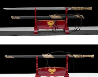Puede incluir: Una espada tradicional con una hoja plateada y un mango dorado adornado, exhibida en un soporte de madera rojo. La vaina negra presenta detalles dorados. El soporte tiene un emblema dorado.