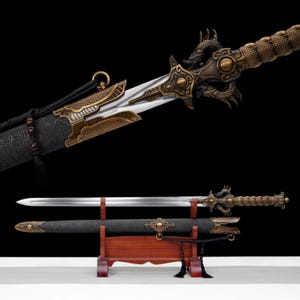 Puede incluir: Una espada ornamentada con una hoja plateada y una empuñadura de color bronce con motivos de dragones. La espada se exhibe con su vaina negra sobre un soporte de madera, mostrando detalles intrincados y artesanía.