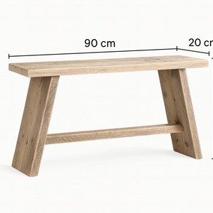 May include: A light-colored wooden bench with a rectangular top and angled legs. The bench is 35 inches long, 8 inches wide, and 18 inches high. The bench has a support beam connecting the legs.