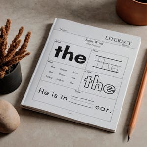 Pode incluir: Um caderno de alfabetiza&ccedil;&atilde;o branco com a palavra "the" em letras grandes e em negrito. O caderno inclui se&ccedil;&otilde;es para tra&ccedil;ar, colorir e escrever a palavra. Um l&aacute;pis est&aacute; ao lado e uma pequena planta est&aacute; ao fundo.