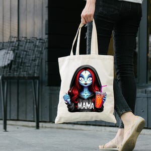 May include: Cream-colored tote bag featuring a cartoon character with blue skin, red hair, and a black hoodie with the word "MAMA". The character is holding a drink with a pink straw. The bag has long handles.